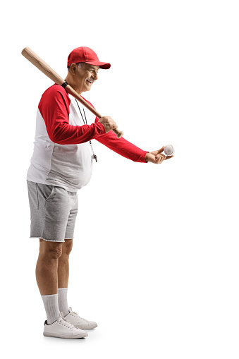 Full length profile shot of a mature man with a baseball bat giving a ball isolated on white background
