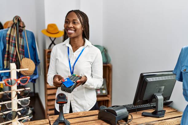 joven comerciante afroamericana usando teléfono de datos y tarjeta de crédito en una tienda de ropa. - owner boutique store retail fotografías e imágenes de stock