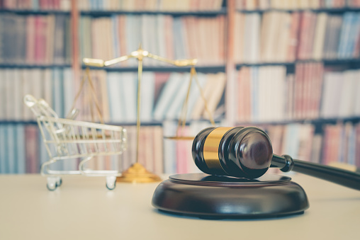 Consumer rights and consimer protection, business law concept : Wooden judge gavel, a shopping cart, a balanced scale of justice on a table, depicting the practice of safeguarding buyers of goods and services.