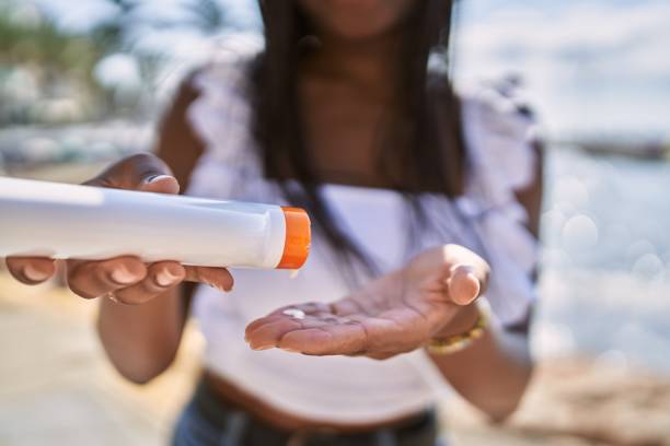 joven afroamericana usando loción de protección solar en la playa. - crema de sol fotografías e imágenes de stock