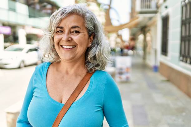 donna dai capelli grigi di mezza età che sorride felice in piedi alla città. - middle aged woman foto e immagini stock