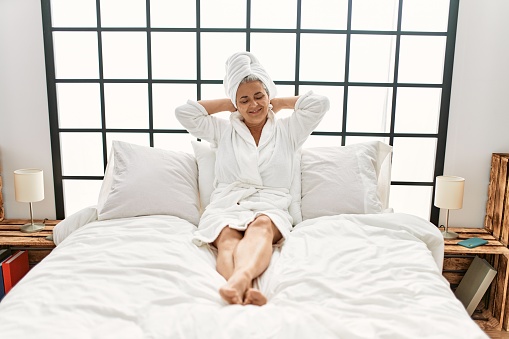 Middle age grey-haired woman smiling happy lying on the bed at bedroom.