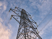 A high voltage electricity transmission pylon - part of the national grid for the distribution of power by overhead cables in the UK. Taken in late afternoon against a blue sky with light clouds.