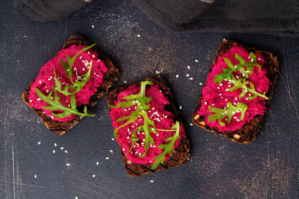 istock Bruschetta with beetroot hummus, arugula and sesame seeds on dark concrete background. Top view 1351851206