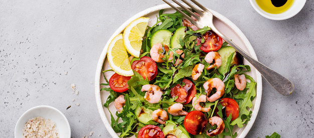 Arugula, cucumber, tomato and shrimp salad with soy sauce on a ceramic plate. Selective focus. Top view.