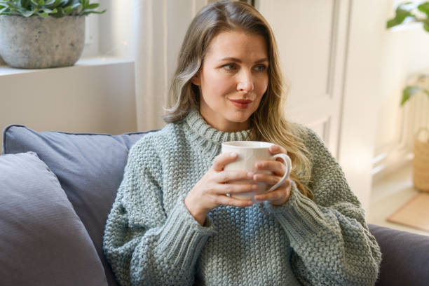 istock attractive middle aged woman sitting on the couch (drinking hot tea) 1351852597