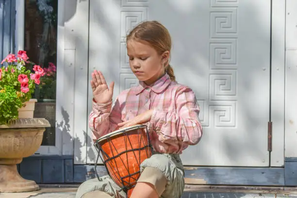 Photo of girl child with a djembe drum outdoor on the porch of the house photo without processing
