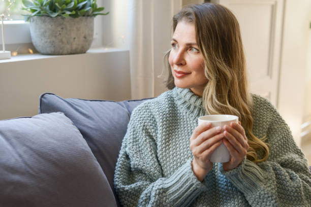 istock attractive middle aged woman sitting on the couch (drinking hot tea) 1351855033