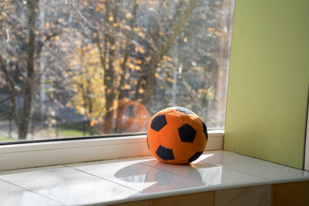 un suave balón de fútbol naranja yace en la ventana. una pelota para clases con niños pequeños. el niño dejó el toy en el alféizar de la ventana - winnie the pooh fotografías e imágenes de stock