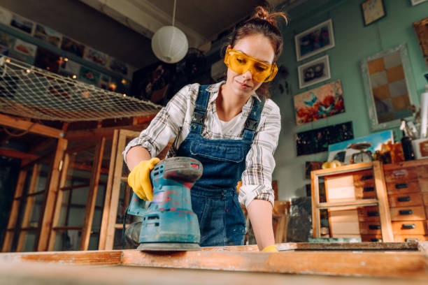 Young woman wearing protective glasses working in the workshop A portrait of a woman wearing protective glasses and gloves working in the workshop using a disc sander. Upcycling concept. power tool photos stock pictures, royalty-free photos & images