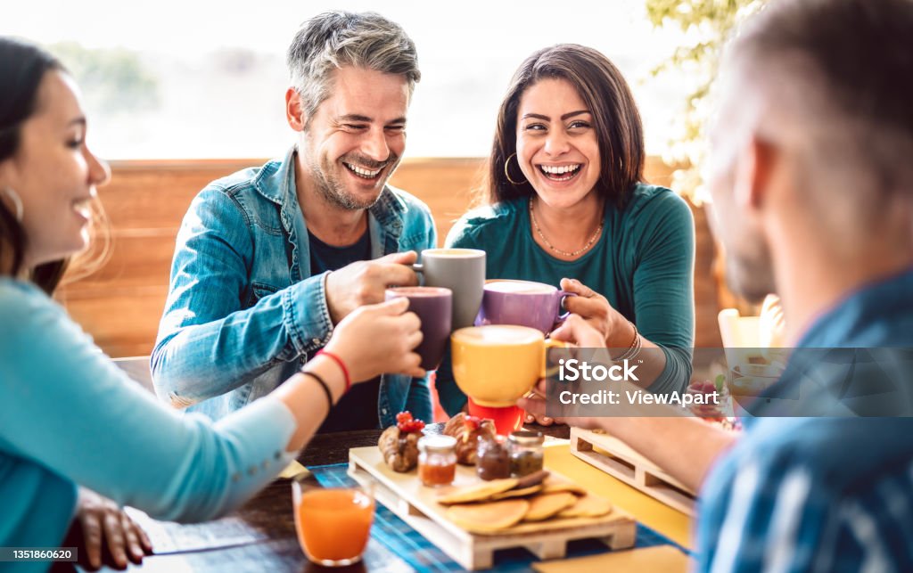 People group toasting latte at coffee bar rooftop - Friends talking and having fun together at cappuccino restaurant - Life style concept with happy men and women at cafe terrace - Bright warm filter Friendship Stock Photo
