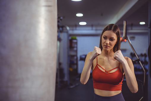 Young woman training punch  for punching bag. Girl making Strong kick. gym.