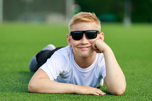 a blonde boy in dark glasses lies on a football field. High quality photo