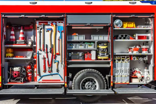 Close-up of the fire engine with various firefighters equipment (water pump, fire extinguishers, nozzles, valves, fire hoses, lighting and signaling equipment, axes, shovel, saw, levers, large pliers...)
