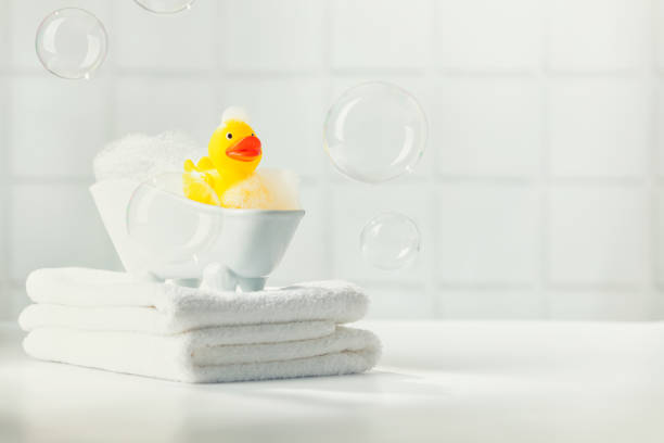 un bagno di bolle in miniatura, anatra di gomma gialla e asciugamani bianchi sul piano di lavoro del bagno, accessori da bagno per bambini, cura del bambino - rubber duck foto e immagini stock