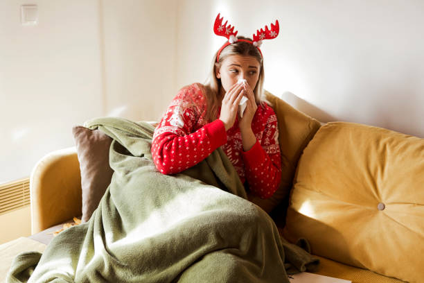 Woman suffering from cold, lying in bed under blanket with tissue during Christmas holidays stock photo