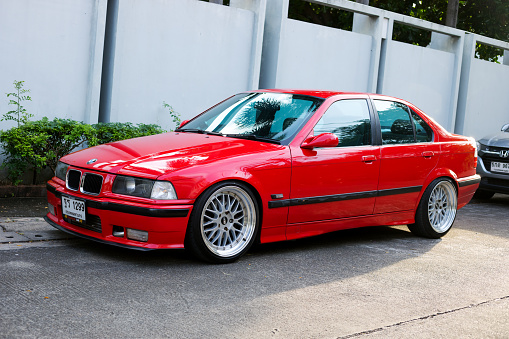 Red colored BMW 325 parked in front of white wall in Bangkok