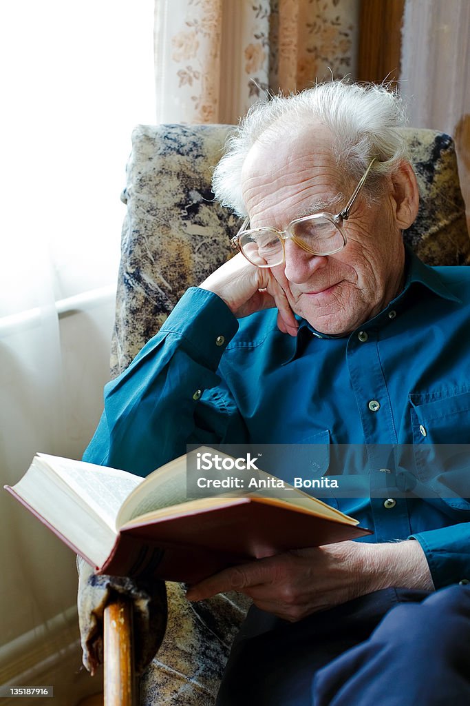 Reading Funny Book smiling old man in glasses reading a funny book, holding his head Active Seniors Stock Photo