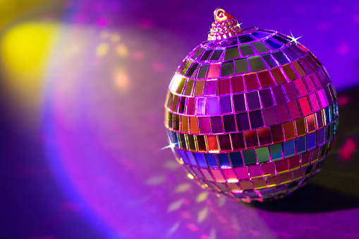 Christmas disco ball with bright ray lights and colorful bokeh on blue neon background. Festive concept for entertainment or celebration.