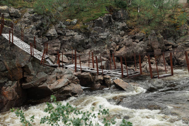 istock Destroyed suspension bridge over a stormy mountain river. River flow in rocky terrain 1351880407