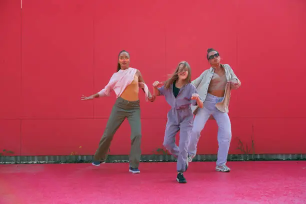 Photo of Dancing girls perform energetic street dance having fun on red background outdoors. Professional hip hop female dancers