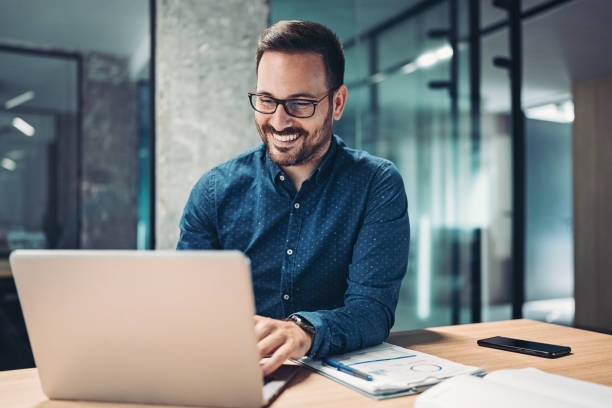 Smiling businessman using laptop in the office stock photo