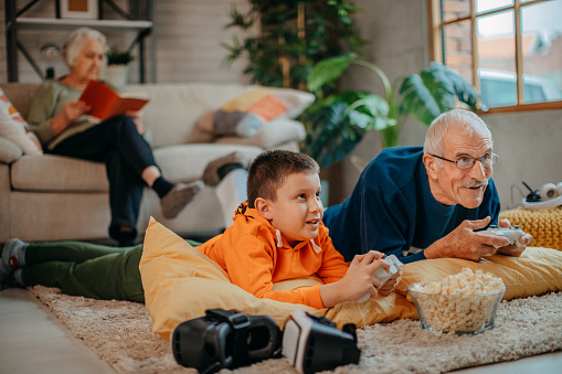 Grandfather playing video games with his grandson in living room on floor