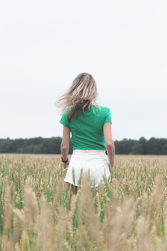 Woman in green t-shirt and white shorts stands with her back in an open field