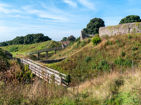 A view of part of the ruins of the keep and defences at Castle Acre Castle in the ancient village of Castle Acre in Norfolk, Eastern England, on a sunny day in September. The motte-and-bailey castle was built by order of William de Warenne during the 1070s near the junction of the River Nar and Peddars Way. Very little is left of the castle now but the village also contains the ruins of a Cluniac Priory and an imposing Bailey Gate, so there is much of interest to see in this now small village, which was once a fortified town.