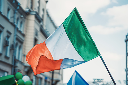 Flag of Ireland close-up on background of blue sky, city street. Saint Patrick day holiday