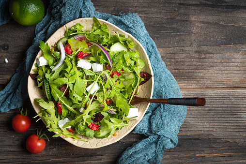 Fresh, spring, arugula salad with feta cheese, red onion, cherry tomato, in a black bowl, on a wooden background. Top view.