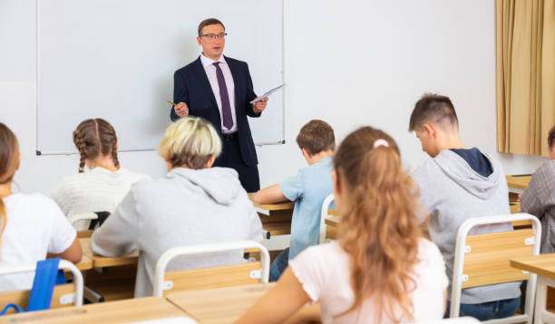 istock Man teacher with notebook is giving interesting lecture for students in classroom 1351892529