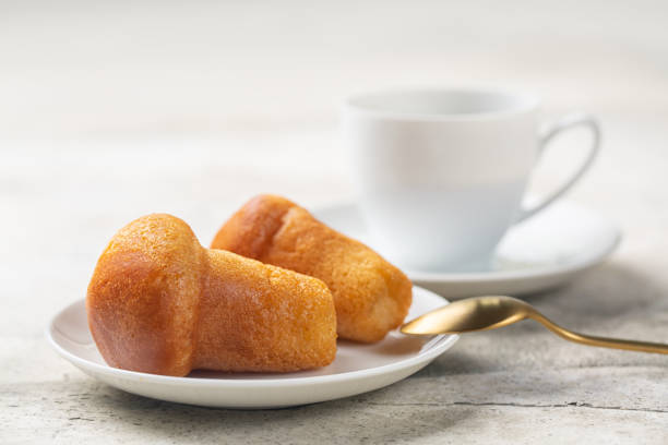 Rum baba or baba au rhum. Small yeast cake saturated in syrup made with rum.  Close-up, selective focus. Coffee cup. Light background. stock photo