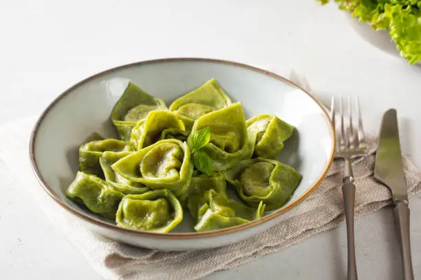 Dinner with homemade tortelli - italian green pasta filled with ricotta and spinach. Light background.