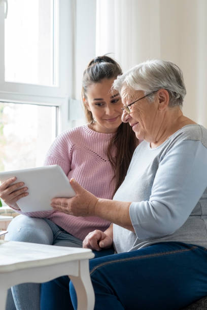 Grandmother and granddaughter Granddaughter and  grandmother  sitting on a sofa at home and  using digital tablet togethernees. doing a favor stock pictures, royalty-free photos & images