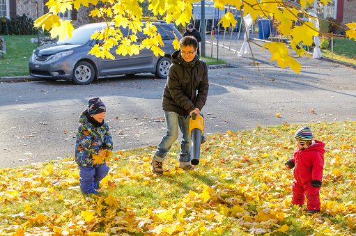 Chinese father playing with kids and leaf blower on the front yard during a day of autumn