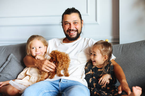 istock Happy father and daughters having fun with their toy poodle on the sofa 1351904908