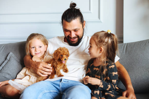 istock Happy father and daughters having fun with their toy poodle on the sofa 1351904946