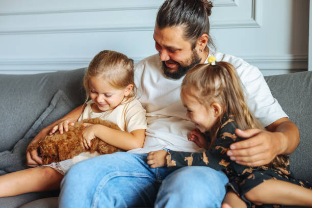 istock Happy father and daughters having fun with their toy poodle on the sofa 1351904971