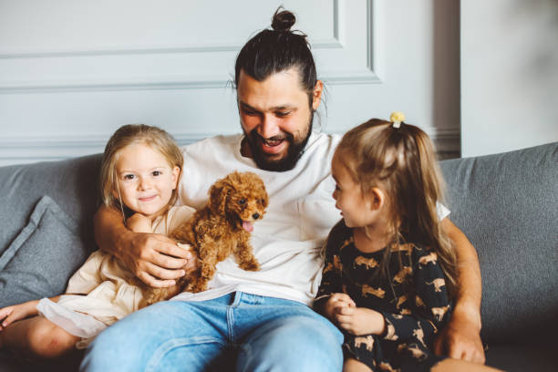istock Happy father and daughters having fun with their toy poodle on the sofa 1351905014