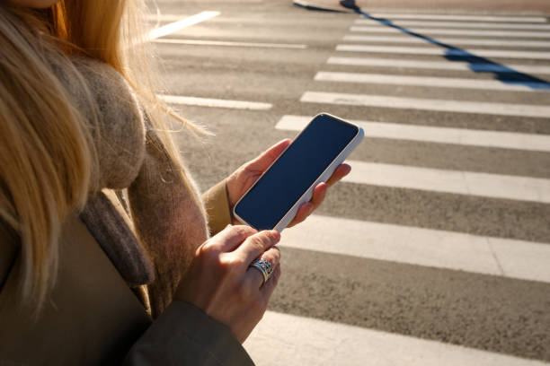 Woman looks at a smartphone while crossing the road. The pedestrian does not follow the road rules. Girl stands at an intersection with a phone in her hands and looks at the screen. Smartphone closeup stock photo