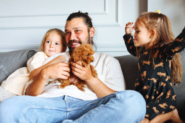 istock Happy father and daughters having fun with their toy poodle on the sofa 1351905052