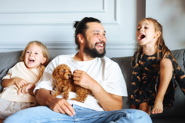 istock Happy father and daughters having fun with their toy poodle on the sofa 1351905077