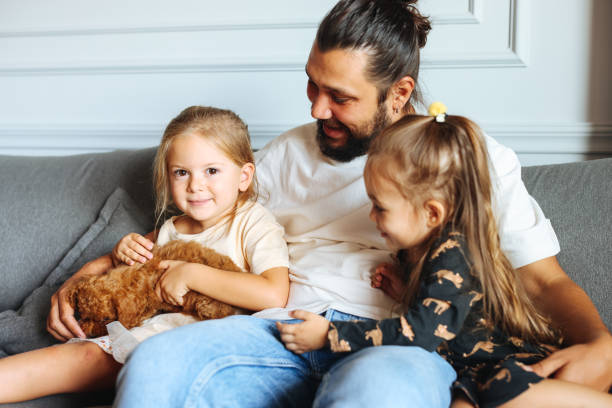 istock Happy father and daughters having fun with their toy poodle on the sofa 1351905117