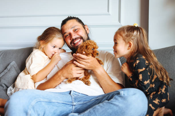 istock Happy father and daughters having fun with their toy poodle on the sofa 1351905135
