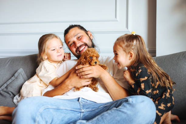 istock Happy father and daughters having fun with their toy poodle on the sofa 1351905166