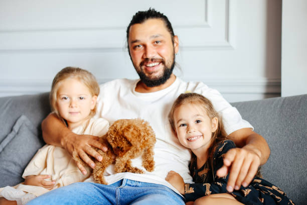 istock Happy father and daughters having fun with their toy poodle on the sofa 1351905189