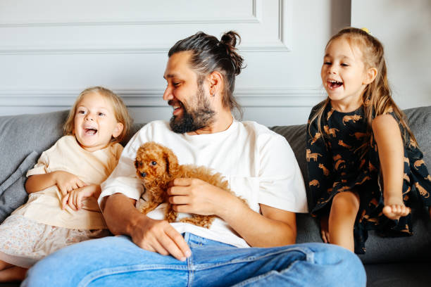 istock Happy father and daughters having fun with their toy poodle on the sofa 1351905218