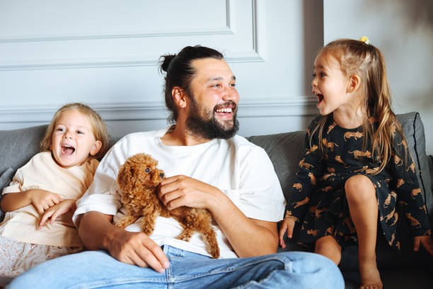istock Happy father and daughters having fun with their toy poodle on the sofa 1351905251