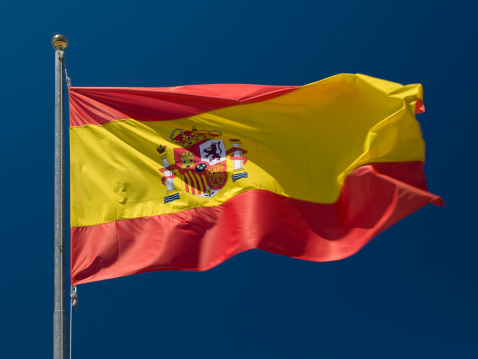 Spanish flag rippling in the breeze against a blue sky without clouds